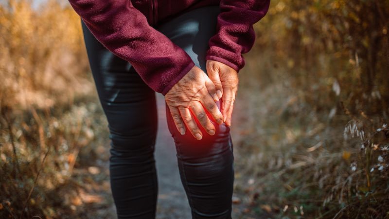 eine person hält sich auf einem herbstlichen wanderweg das schmerzende knie