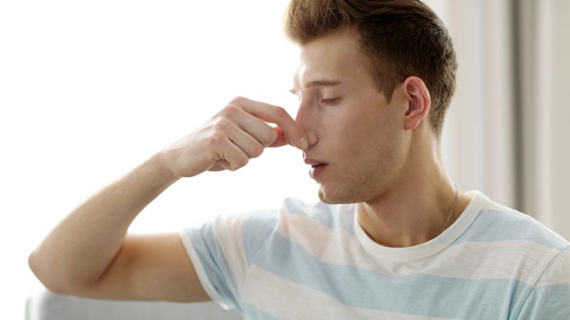 junger mann greift sich auf die nase